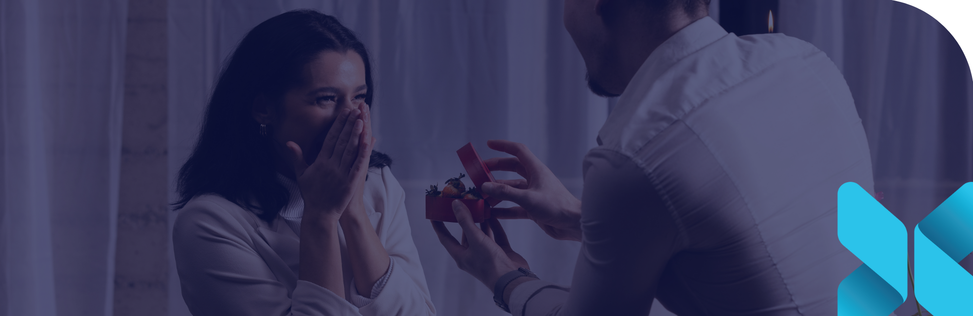 man kneeling infront of a woman in joyful shock as he holds a heart shaped box full of strawberries